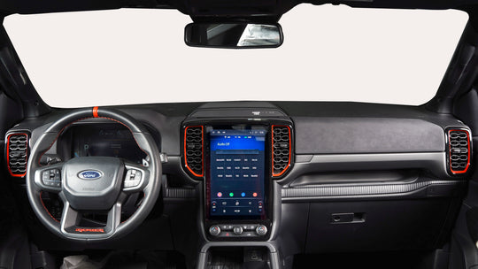 A Ford truck interior dashboard featuring a large central touchscreen display, a wrapped steering wheel with orange stitching, and custom black and orange air vent trim.
