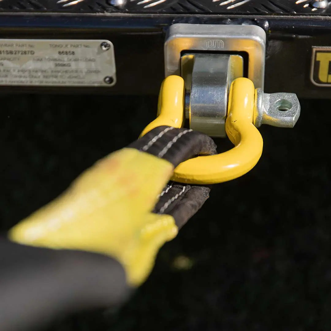 Hand wearing a yellow glove securing a yellow shackle to a vehicle's hitch receiver.